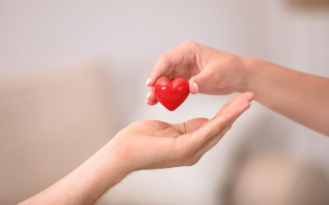 Person giving red heart to another on a blurred background, closeup.